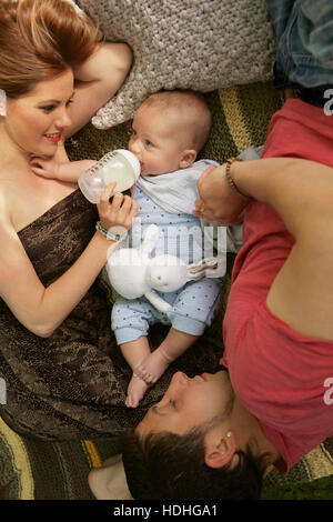 Directly above shot of woman feeding baby boy with bottle while man lying on bed at home Stock Photo