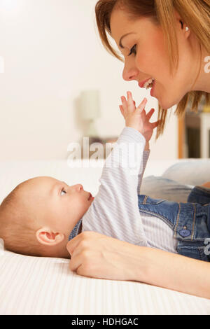 Cute baby boy reaching hands towards mother while lying on bed at home Stock Photo