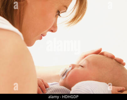 Loving mother looking at baby boy sleeping on bed Stock Photo
