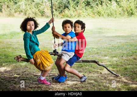 Two boys and a girl sitting on a tree swing. Stock Photo