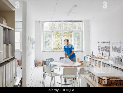 A modern office. A man looking at plans at a table, architectural drawings. Building models on shelves. Open windows. Summer. Stock Photo