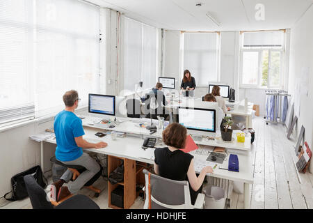 A modern office, workstations for staff. Elevated view of six people seated at desks. A man using an ergonomic kneeler chair. Stock Photo