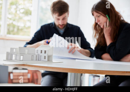 A modern office. Two people at a meeting discussing plans and architectural drawings. A small-scale model building in the foreground Stock Photo