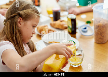 A family having breakfast. A girl pouring orange juice into a glass. Stock Photo