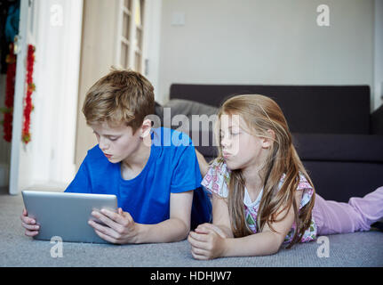 Two children lying on their stomachs sharing a digital tablet watching the screen. Stock Photo