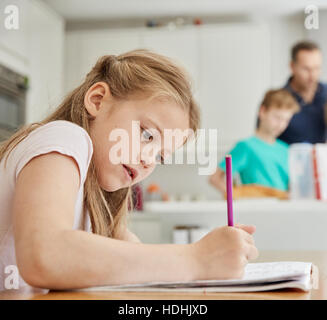 A girl sitting at a table in the family kitchen, holding a pencil, doing her homework. Stock Photo