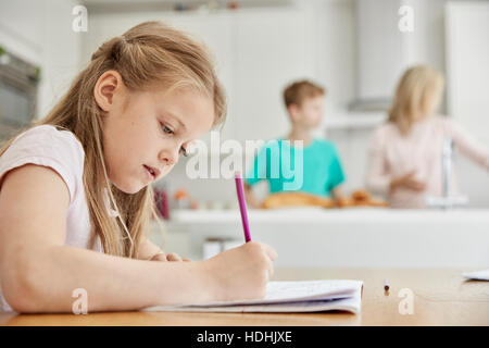 A girl sitting at a table in the family kitchen, holding a pencil, doing her homework. Stock Photo