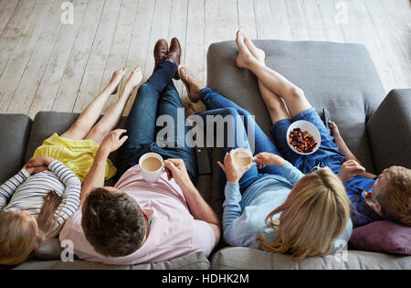 A family at home.  View from above of two adults and two children seated on a sofa together. Stock Photo