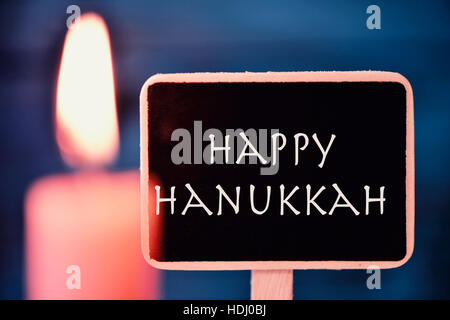 closeup of a black signboard with the text happy Hanukkah, for the Jewish Festival of Lights, and a lit candle Stock Photo