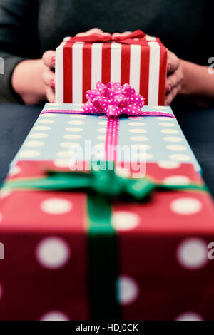 closeup of some gifts wrapped in colorful papers and tied with ribbons of different colors and a young caucasian woman grabbing one of them in the bac Stock Photo