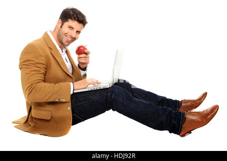 sitting man working on computer while holds an apple in his hand Stock Photo