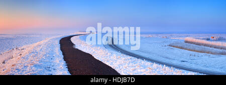 Sunrise over a dike along a frozen lake on a record-breaking cold morning near Uitdam in The Netherlands. Stock Photo