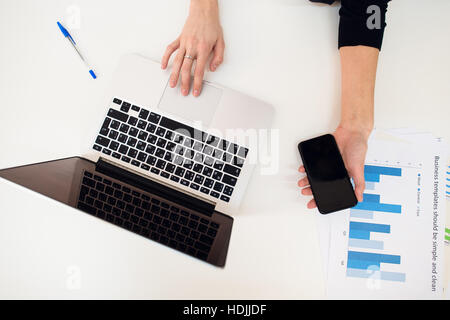 Laptop with women hand and paper graph on white table. Stock Photo