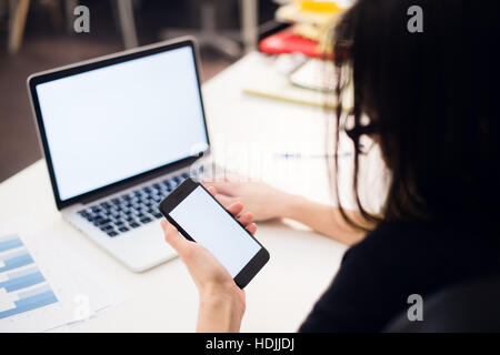 Woman's hands using mobile phone and laptop at the office Stock Photo