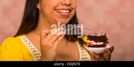 Brunette woman holding small plate of chocolate cake with cream filling, grabbing bite using fork, showing to camera, pastry concept Stock Photo