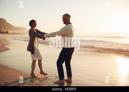 Full length shot of romantic senior couple holding hands and enjoying a day at the beach. Mature couple enjoying themselves on the beach. Stock Photo