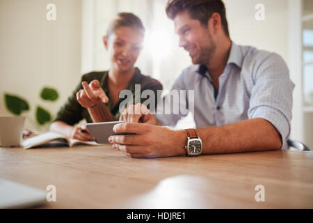 Shot of young couple sitting together at table using smart phone. Young man showing something to his girlfriend on mobile phone. Focus on man hands ho Stock Photo