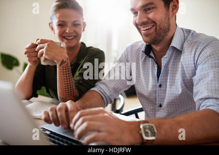 Shot of happy young couple sitting together at table and working on laptop. Smiling man and woman at home using laptop. Stock Photo