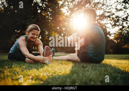 Caucasian couple doing their stretches in park. Fit young man and woman exercising in morning. Stock Photo