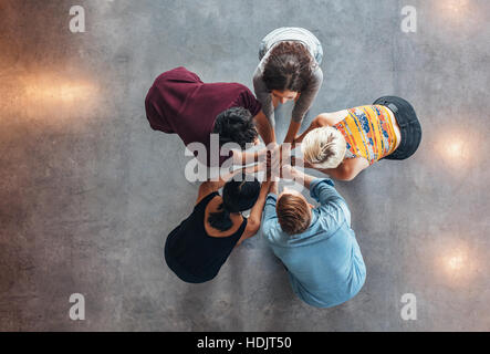 Top view of group of young people putting their hands together. Young students standing in a circle making stack of hands showing success. Stock Photo