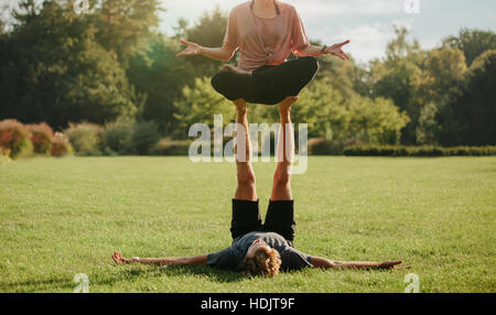 Strong young couple doing acroyoga outdoors. Man and woman in park practising pair yoga poses. Stock Photo