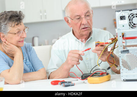 Retired man testing computer with multimeter Stock Photo