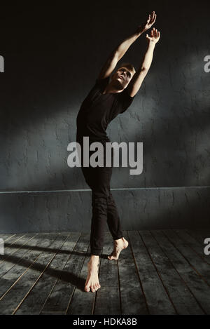 Talented young guy dancing in the black colored studio Stock Photo