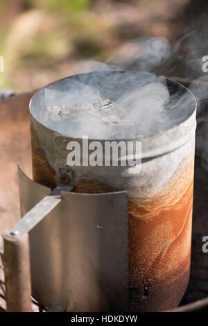 Chimney starter and smoke. Barbecue preparation with charcoal on fire. Stock Photo