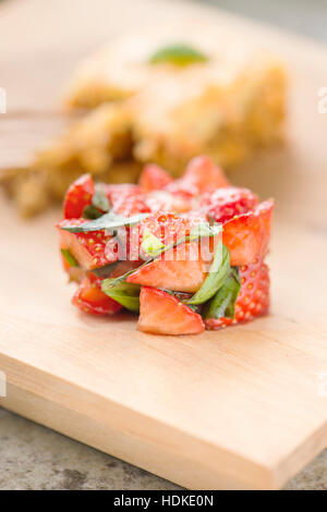 Strawberries and fresh basil leaves marinated in balsamic vinegar. Carrot cake in the background. Stock Photo