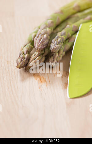 Green asparagus. Uncooked vegetables on wooden kitchen table. Fresh harvest of spring vegetable. Stock Photo