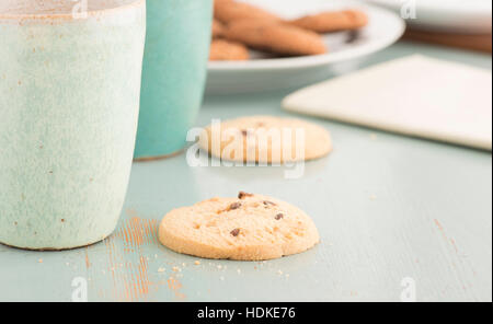 Chocolate chip cookies and coffee or tea mugs. Sweet food, dessert or snack. The cookies are served on a kitchen table. Stock Photo