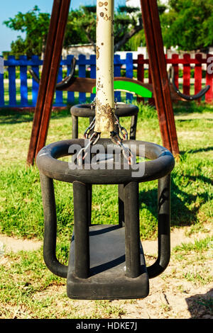 Swing in the playground with colored fences in the background. Vertical image. Stock Photo