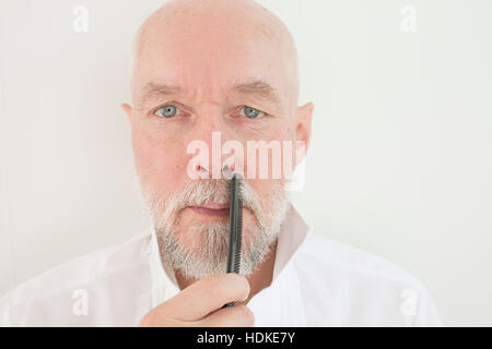 Old man combing beard and mustache with comb. Serious senior adult taking care of his facial hair. Stock Photo