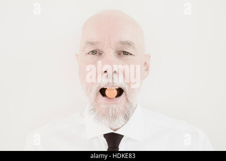 Portrait of old man with small tomato in his mouth. Funny and playful moment. Conceptual image of healthy lifestyle and eating vegetables as a senior Stock Photo