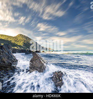 Slow shutter photo of waves breaking onto rocks on the coast of the Desert des Agriates in north west Corsica with dramatic clouds above Stock Photo