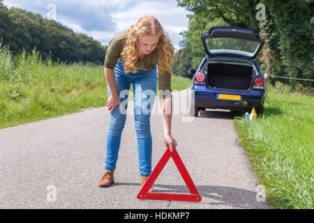 European teenage girl placing hazard warning triangle on country road Stock Photo