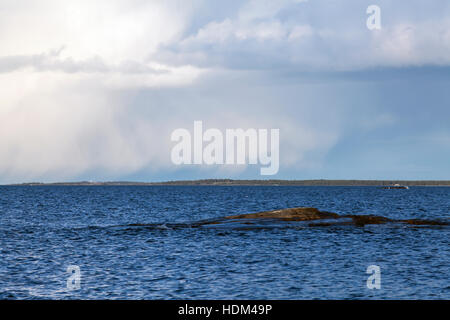 Shower at sea. Rain, hail and snow. Water, waves and rough weather. Rocks this side. Island in the background. Stock Photo