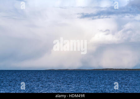 Shower at sea. Rain, hail and snow. Water, waves and rough weather. Island in the background. Stock Photo