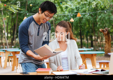 Happy asian man in glasses standing and teaching pretty young woman outdoors Stock Photo