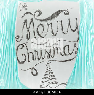 Merry Christmas hand drawn lettering with charcoal on blackboard framed by cyan curtains. Elegant unique design with snowflakes and Christmas tree. Stock Photo