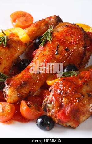 Fried chicken legs in tomato sauce with peppers, olives and rosemary on a white plate, vertical macro Stock Photo