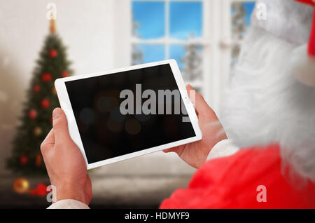 Santa Claus work on tablet with blank screen for mockup. Christmas tree in background. Stock Photo