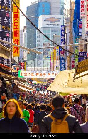 People walking down bustling Namdaemun Market pedestrian shopping street surrounded by stores, signs and crowded with shoppers. Stock Photo