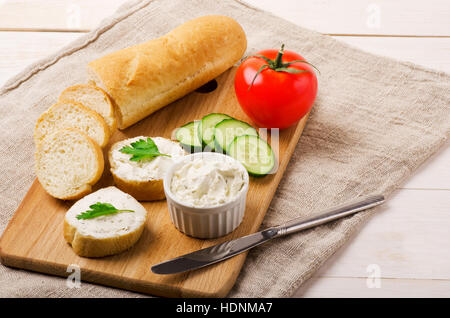 Crunchy baguette slices with cream cheese and vegetables on a cutting board Stock Photo