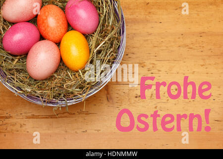 Text Happy Easter in german, Frohe Ostern, with 6 Easter Eggs in a basket with straw on a vintage wooden background Stock Photo