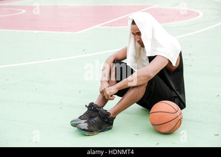 Photo of young tired african basketball player sitting in the park with towel. Stock Photo