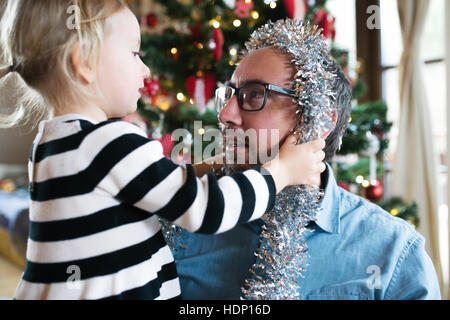 Father with daugter decorating Christmas tree. Silver tinsel on Stock Photo