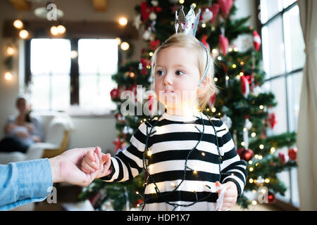 Father with daugter tangled up in light chain at Christmas tree. Stock Photo