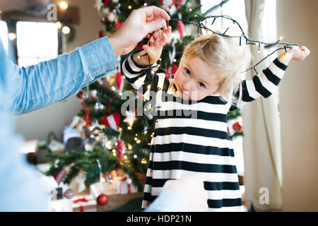 Father with daugter tangled up in light chain at Christmas tree. Stock Photo