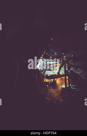 Industrial worker welding round pipe on a work table, producing smoke, sparks and colorful reflections Stock Photo